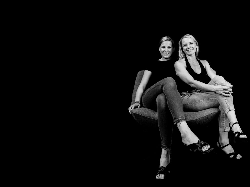 Sabrina und Yvonne, die Gründerinnen von INVISIBLE Weinheim, in Schwarz-Weiß auf einem Sessel